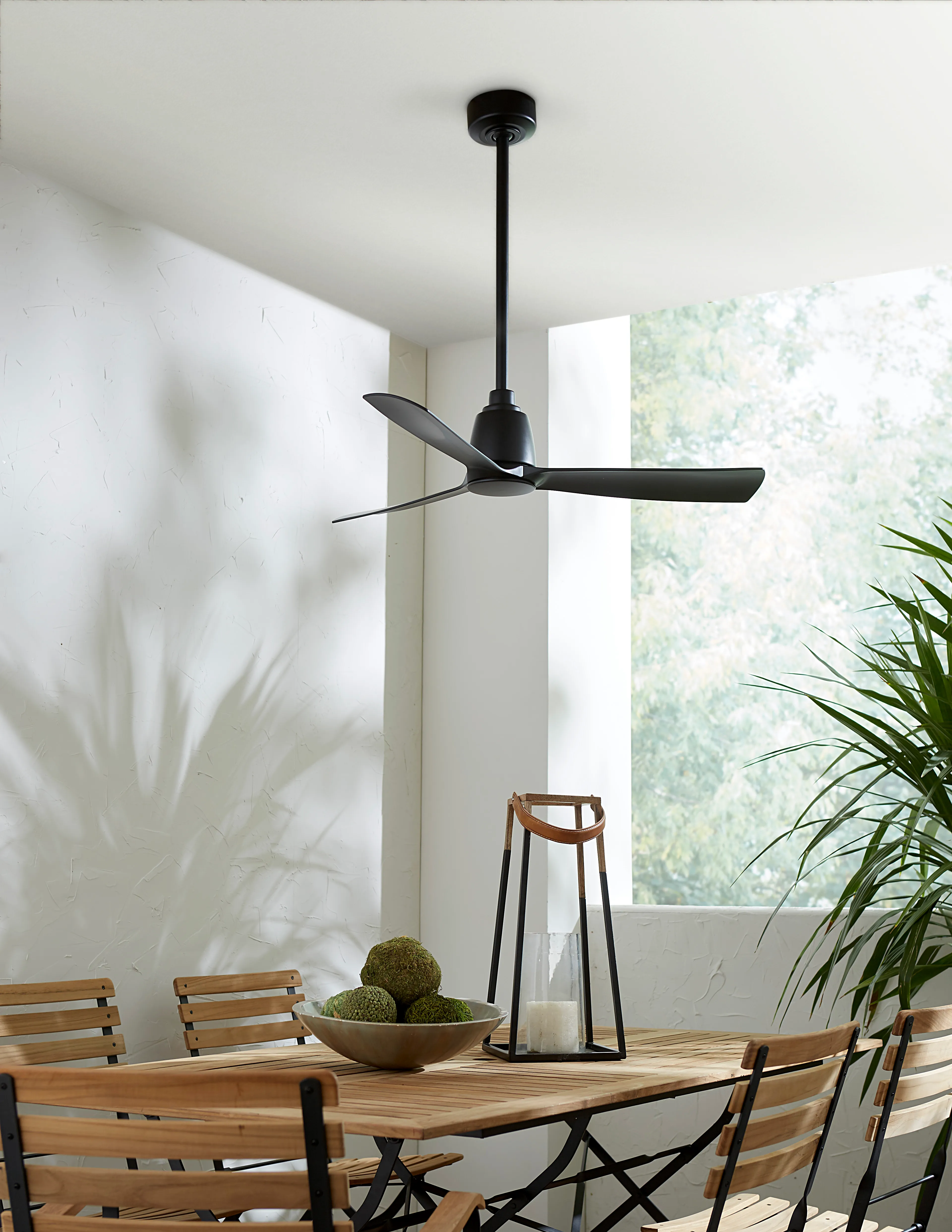 Ventilador de techo moderno negro de tres aspas en un comedor de muros blancos con luz natural